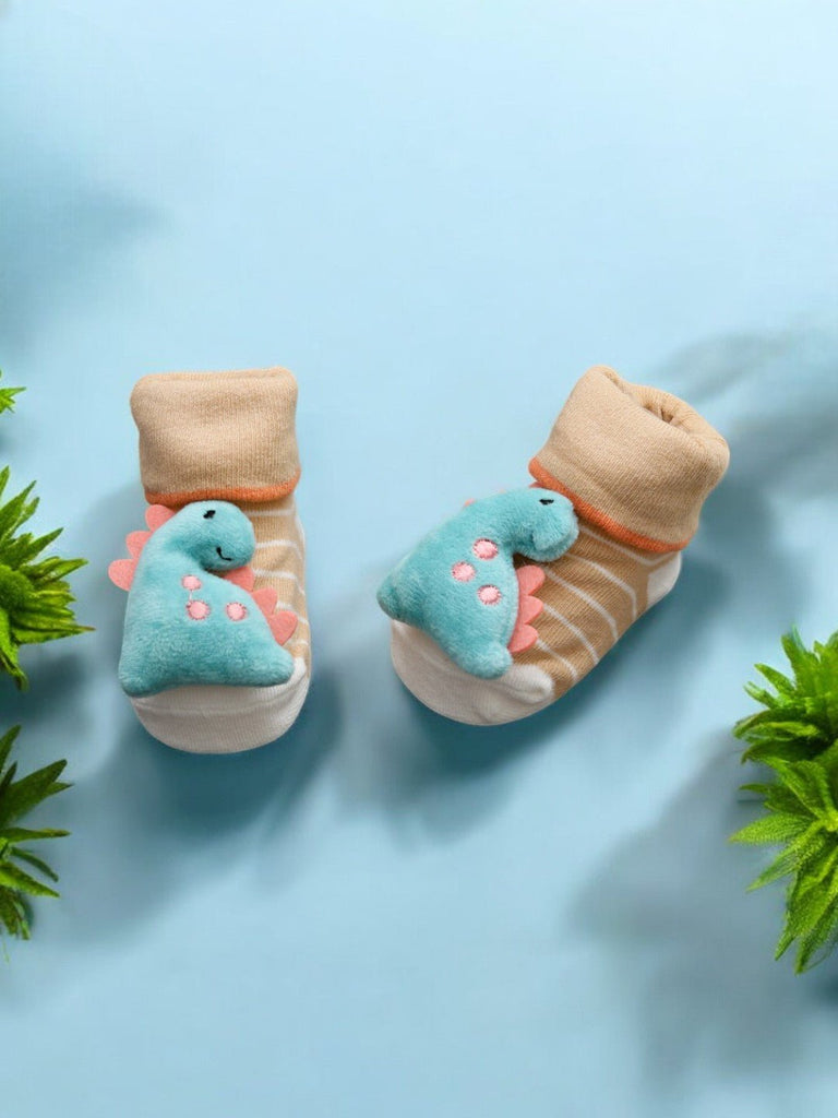 Pair of baby socks with plush dinosaur, creatively displayed on a blue background with greenery - Creative Day