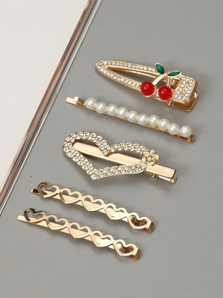 An elegant set of Yellow Bee hair clips displayed on a mirror surface, featuring rhinestone and pearl heart designs, and a cherry accent clip.