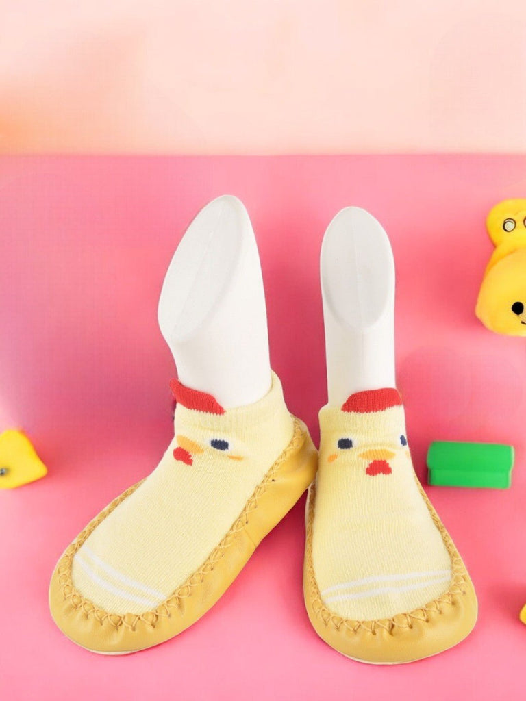 Baby moccasin socks with chick face design in yellow and red, displayed creatively against a backdrop.