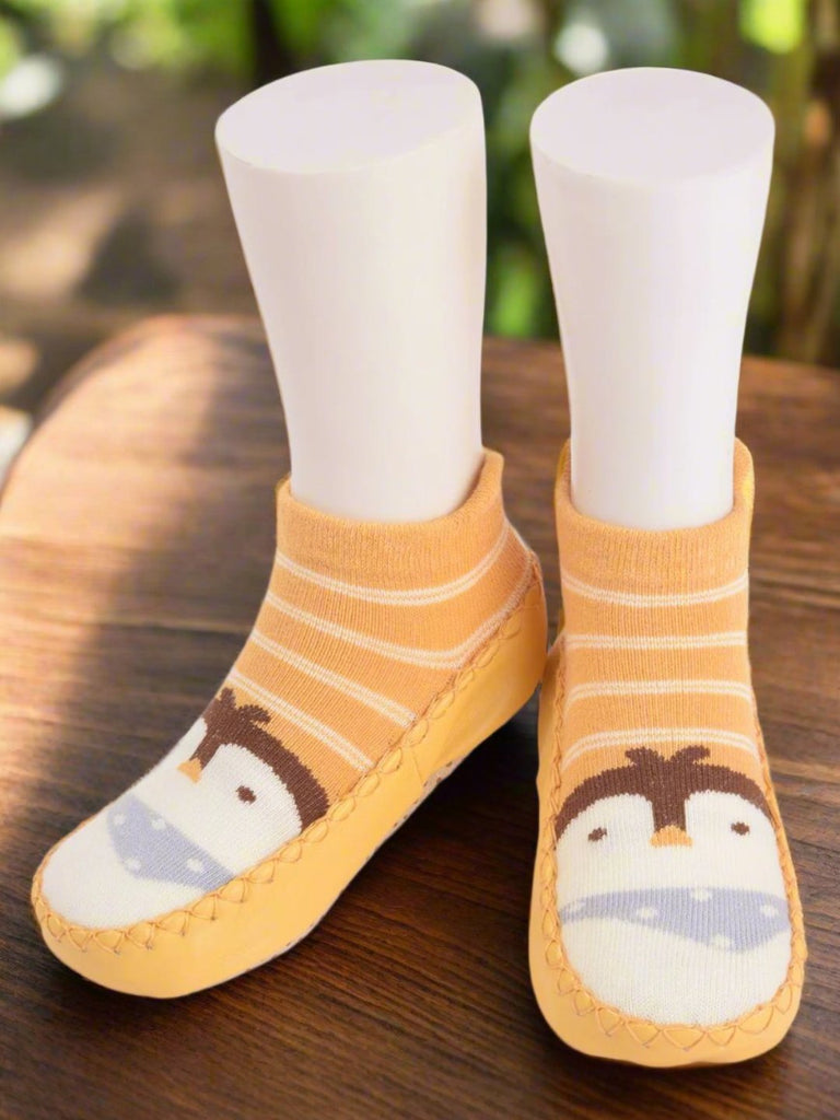 Yellow baby sock shoes with penguin design displayed on a mannequin foot.