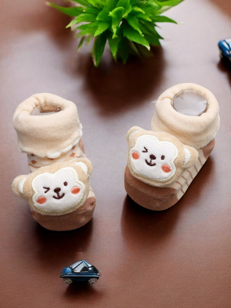 Creative display of beige baby booties with a 3D monkey face, designed to keep babies’ feet warm and stylish.