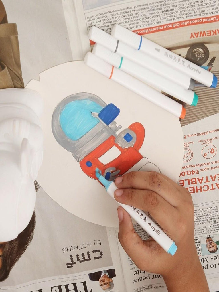 A child coloring the astronaut ceramic figure with acrylic markers.