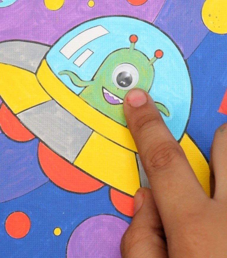 Close-up of a child's hand decorating an astronaut design in the Yellow Bee Cosmic Adventure DIY Art Kit.