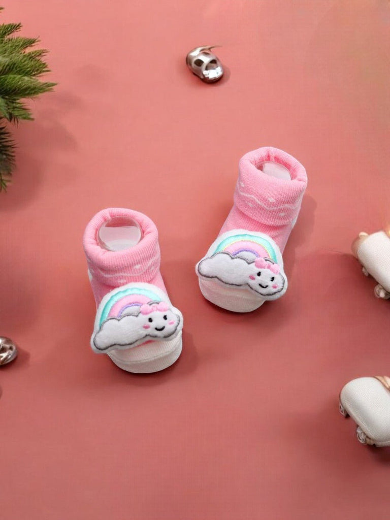 Creative display of pink baby booties with a 3D rainbow and cloud, soft and playful for babies.