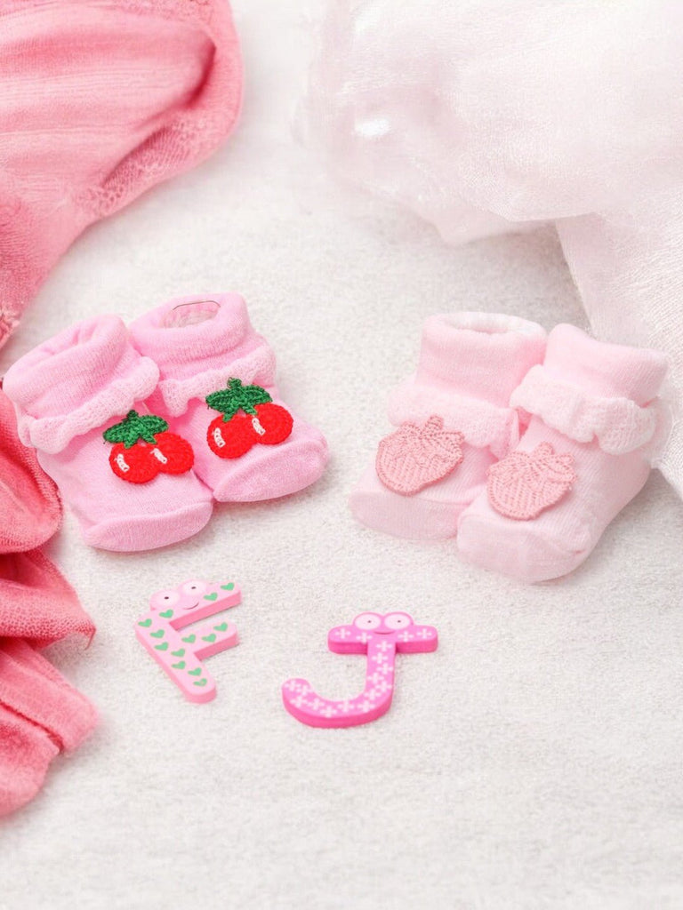 Baby girl's pink socks set with cherry and mango motifs, accompanied by playful number and letter toys.