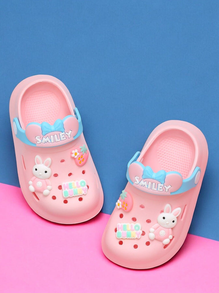 Pair of pink bunny motif clogs for kids with blue 'SMILEY' strap on pastel background.