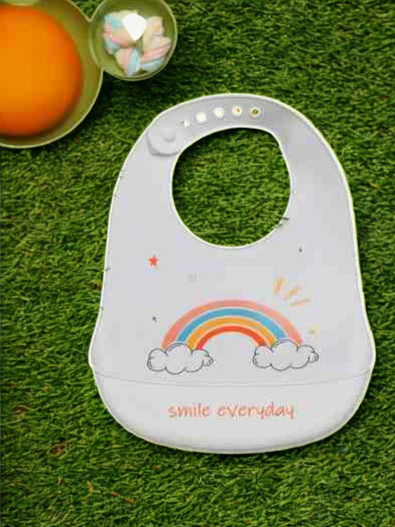 Display of Rainbow Smile Silicone Baby Bib for Girls showing the full bib on a grassy background.