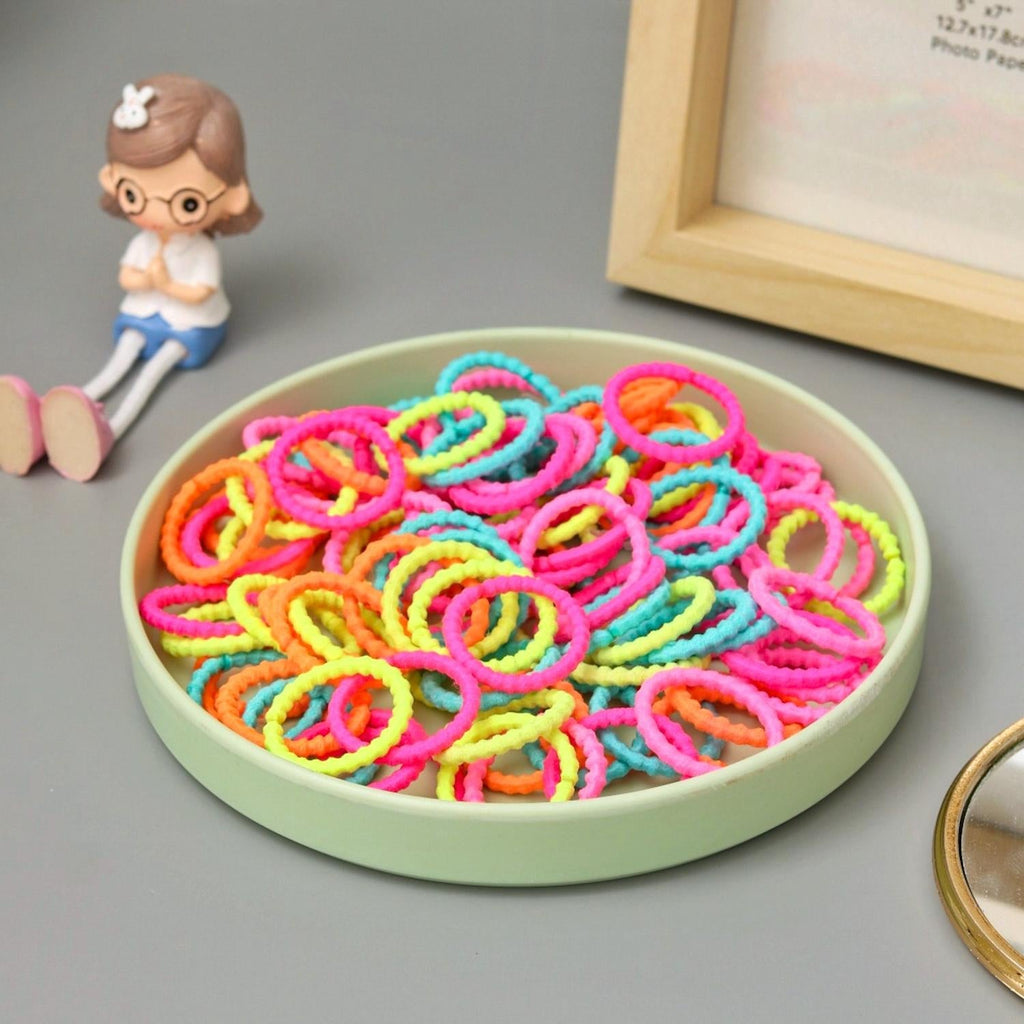 A stylish display of Yellow Bee's 100 colorful hair ties in a dish, with a whimsical character for scale