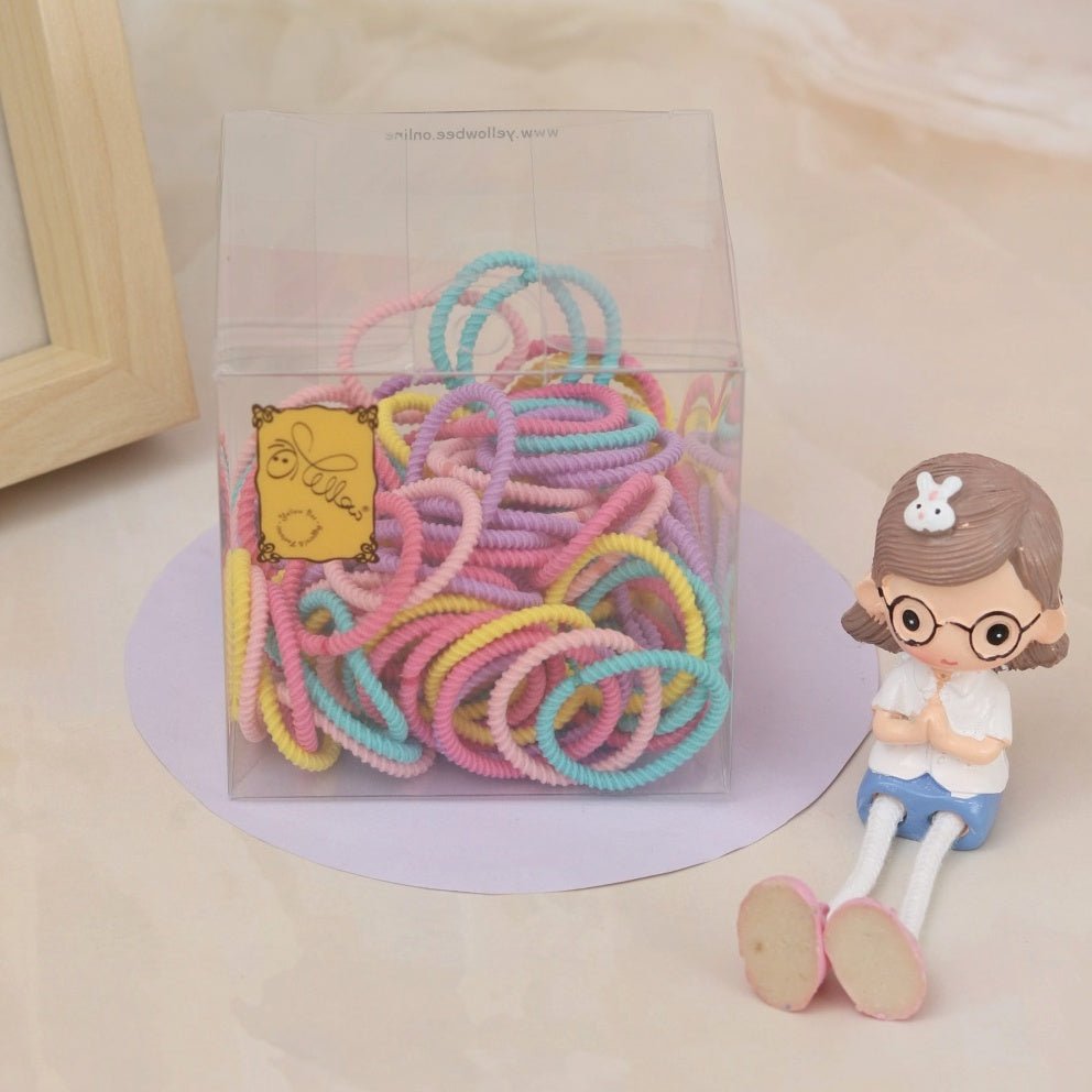 Colorful braided hair ties by Yellow Bee displayed in a clear box with a charming child figurine.