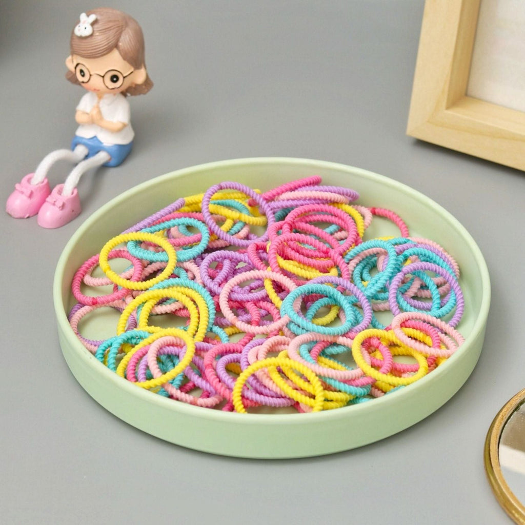 Styled image of Yellow Bee's vibrant multi-colored braided hair ties in a pastel dish.