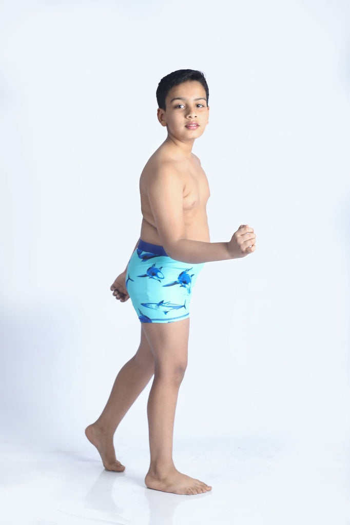 Boy striking a pose in aqua shark print swim shorts by Yellow Bee