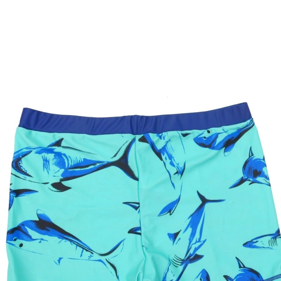 Boys' Yellow Bee swim shorts featuring an aqua shark print, laid flat on grass with summer accessories.