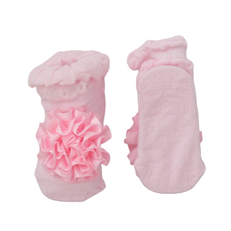 Bottom view of pink baby girl socks with ruffled flower detail, showcasing non-slip soles.