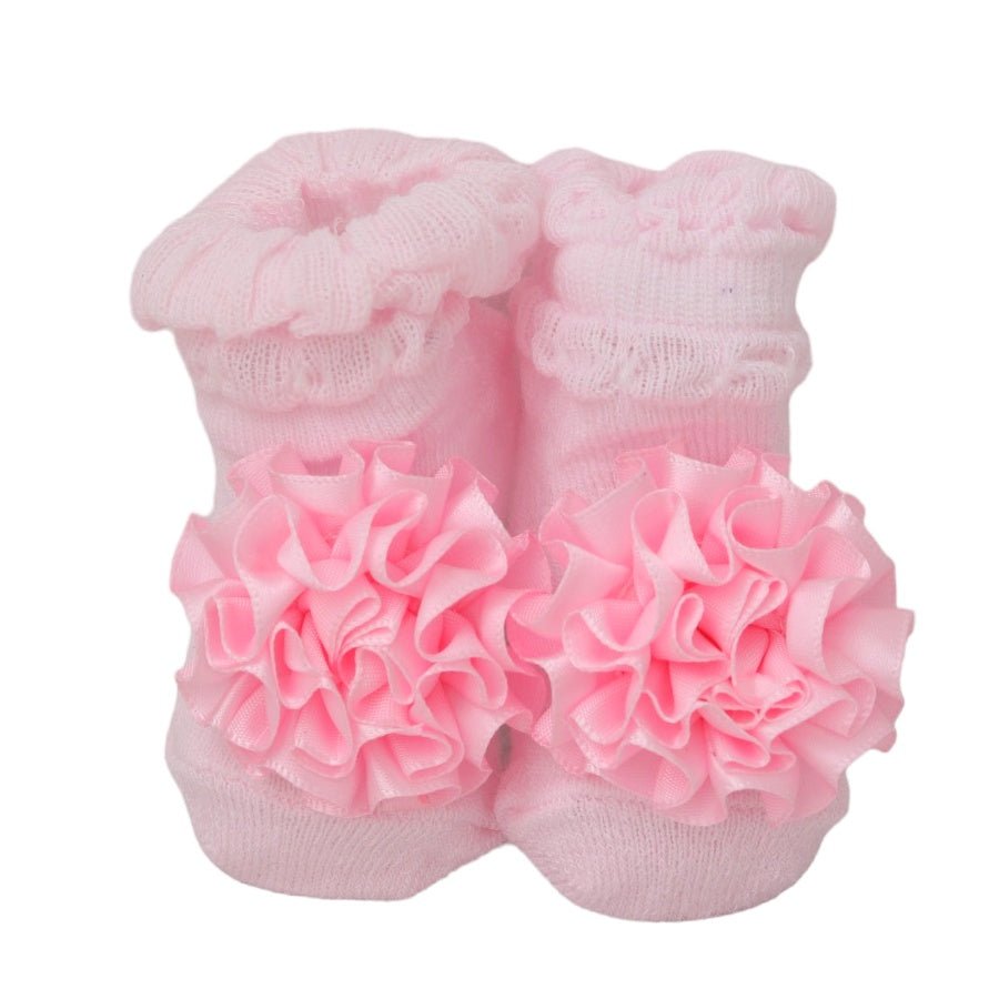 Close-up of pink baby girl socks with large ruffled flower decorations.