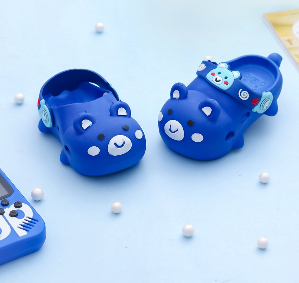 Children's blue clogs with a bear pattern and decorative charms on a playful background.