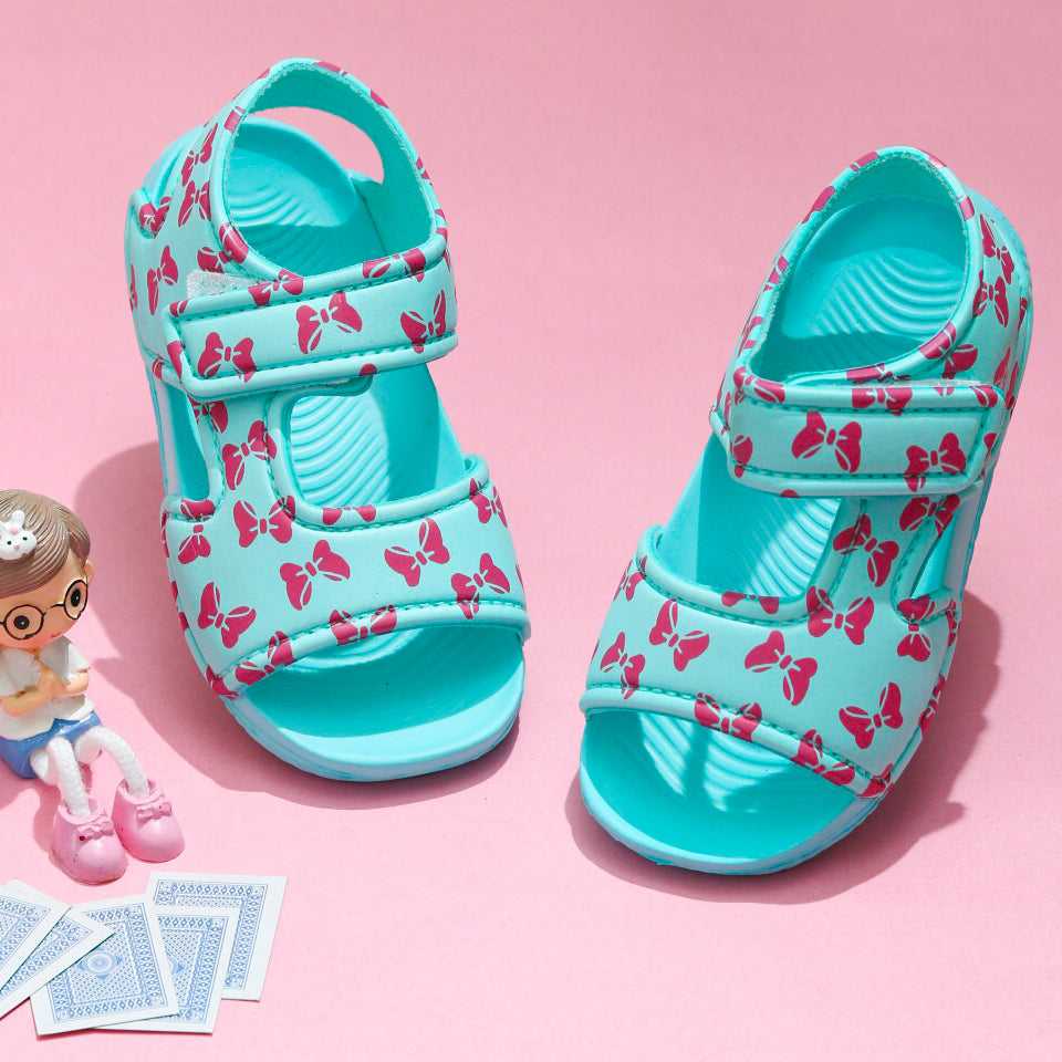 Child's aqua sandal with playful pink bow prints on a pink background