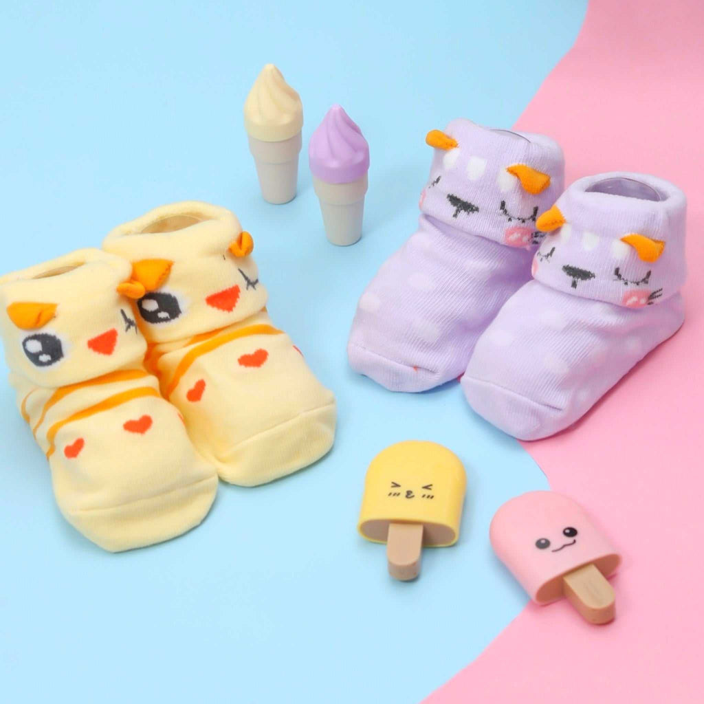 Two pairs of Yellow Bee's animal-themed anti-skid socks in yellow and purple, displayed among playful toy ice creams on a pastel background.