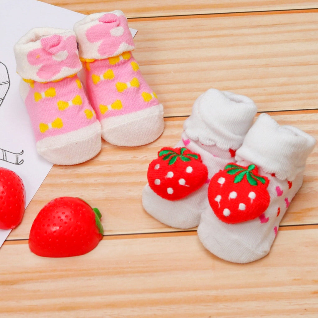 Pink and white baby socks with flower and strawberry designs on wooden background.