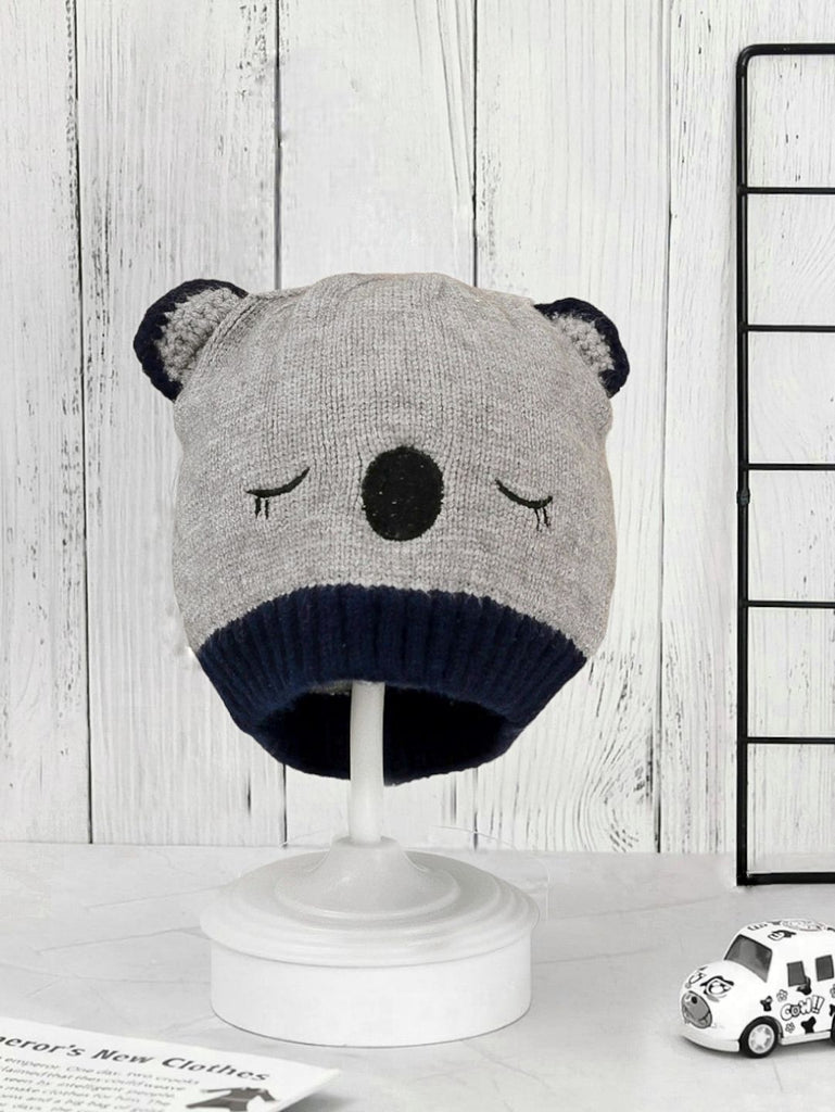 White knitted beanie with brown bear features on display stand.