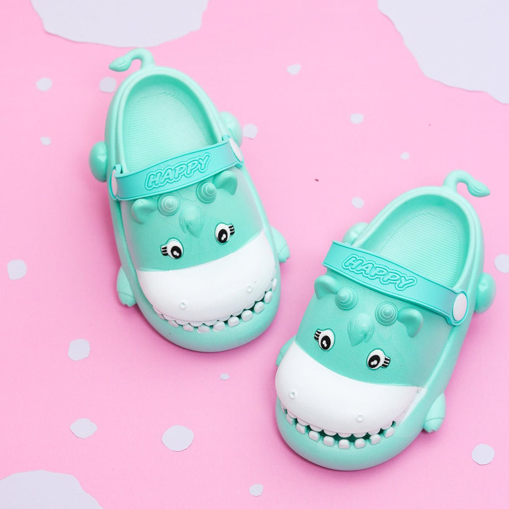 Pair of aqua-colored hippo pattern clogs for toddlers on a pink polka dot background