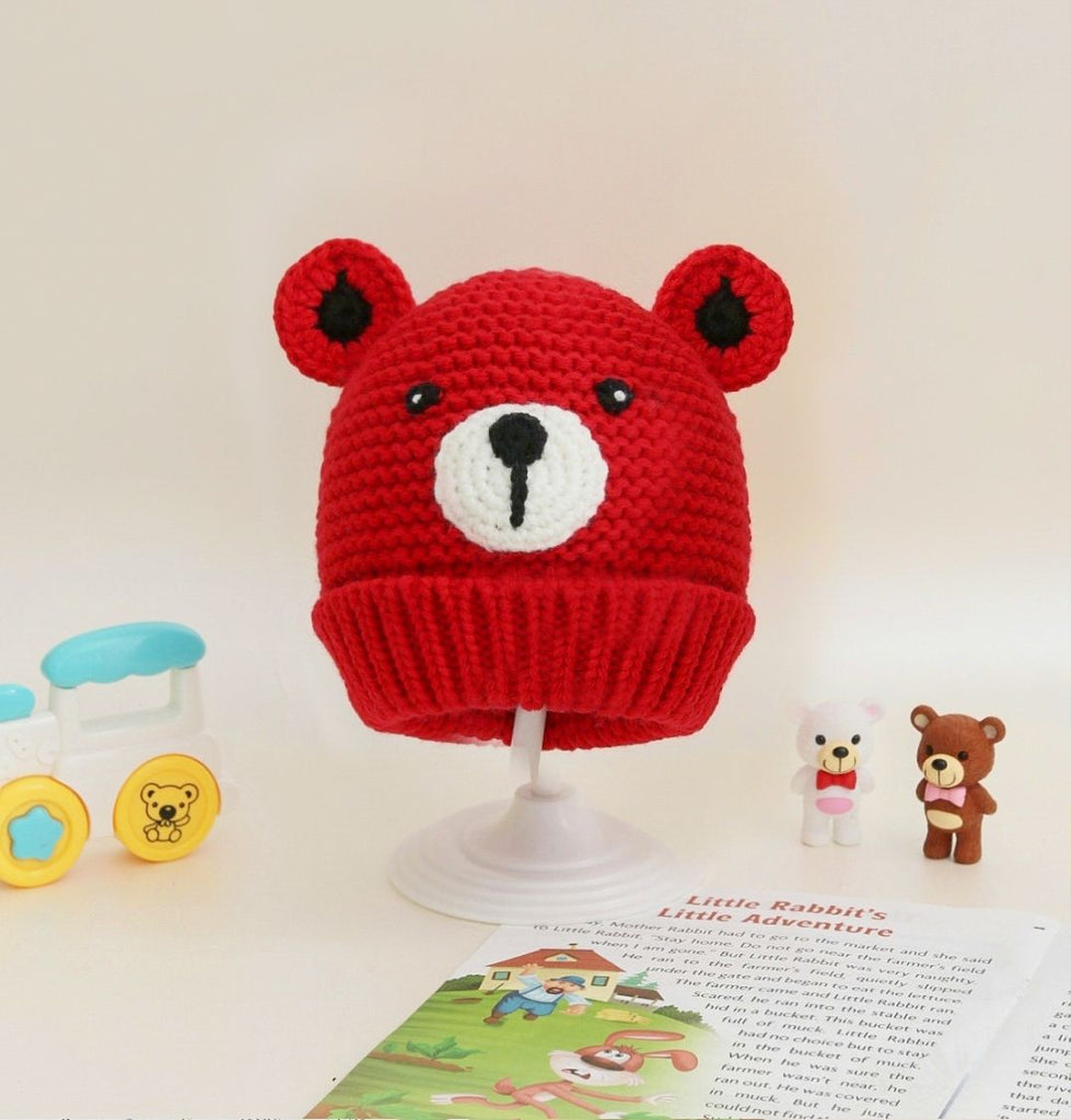 Bright red crochet woolen beanie with teddy bear design for baby girls on display.