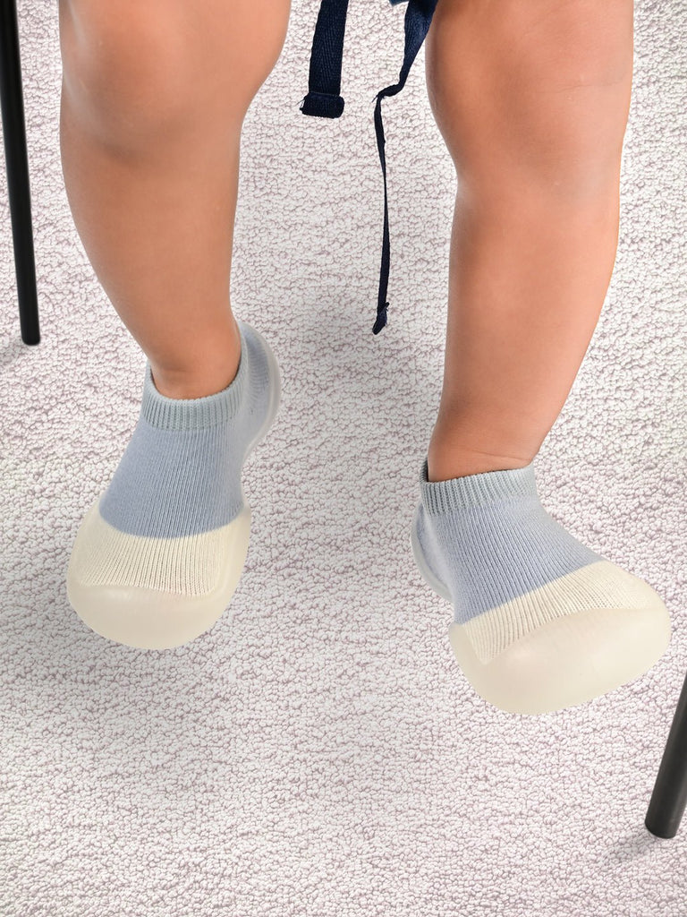 Toddler wearing grey Yellow Bee shoe socks with anti-skid sole on a textured background.