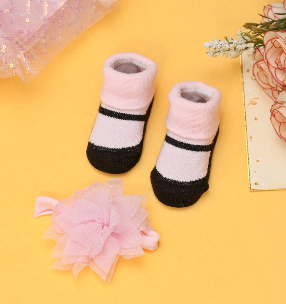 Pink and black baby socks with coordinating pink headband on a yellow background.
