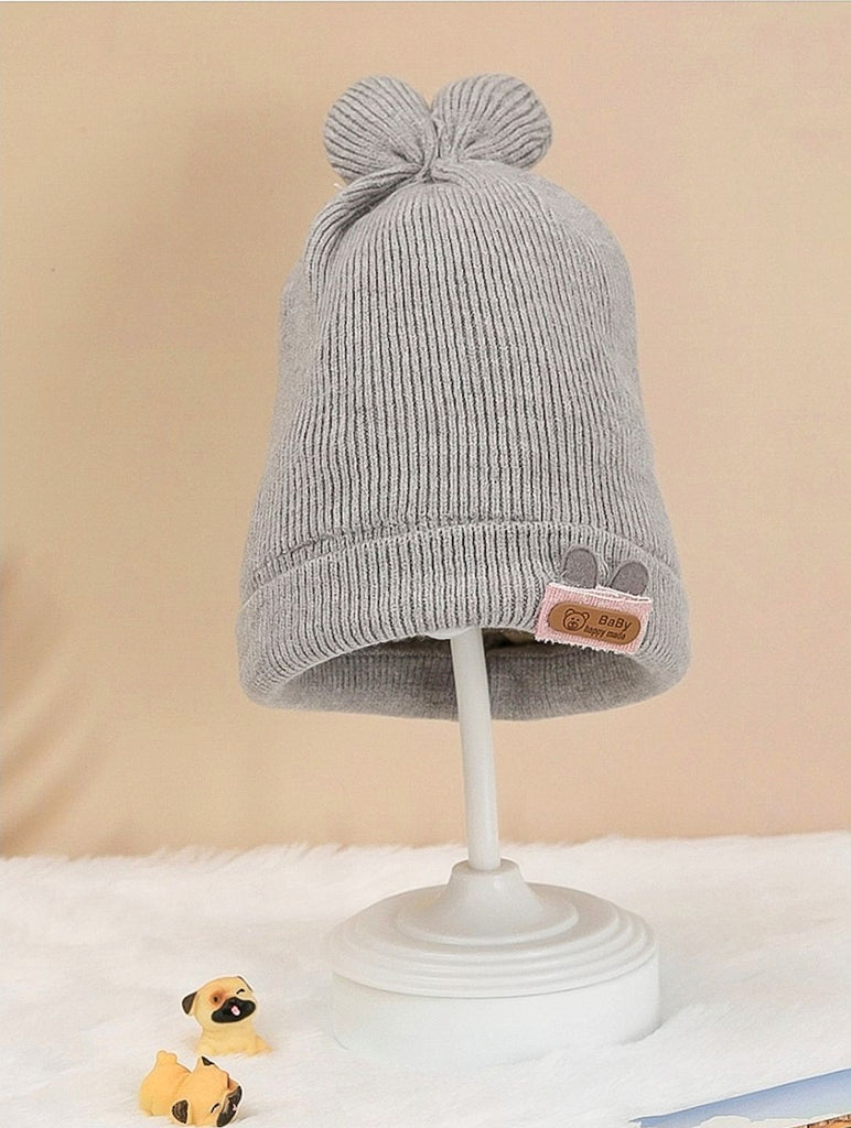 Grey woolen toddler cap with a fluffy pom-pom on a display stand