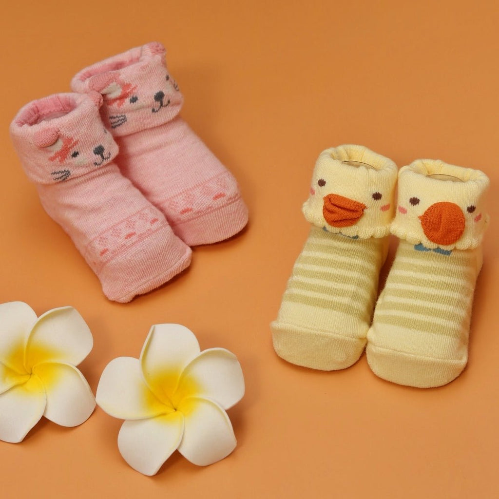 Two pairs of baby girl socks with cat and duck designs on an orange background with flowers.