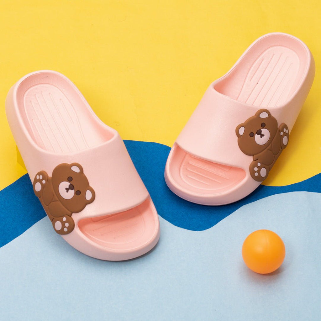 Kids' peach-colored slides with teddy bear embossment on top against a yellow and blue background.
