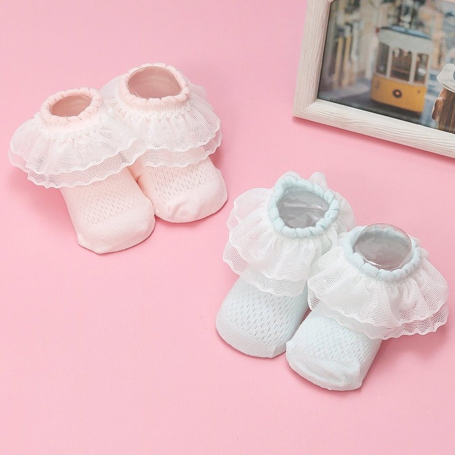 Yellow and white baby girl's leather socks with lace frill displayed on a pink background.
