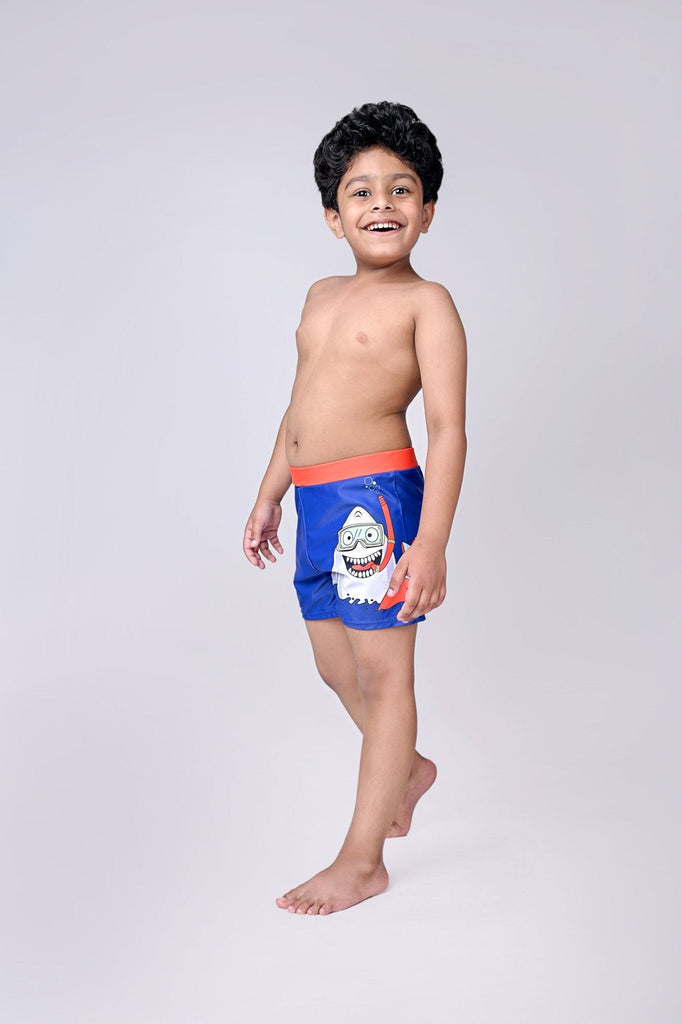 Young boy smiling in blue shark-themed swim shorts with snorkel design, ready for summer fun