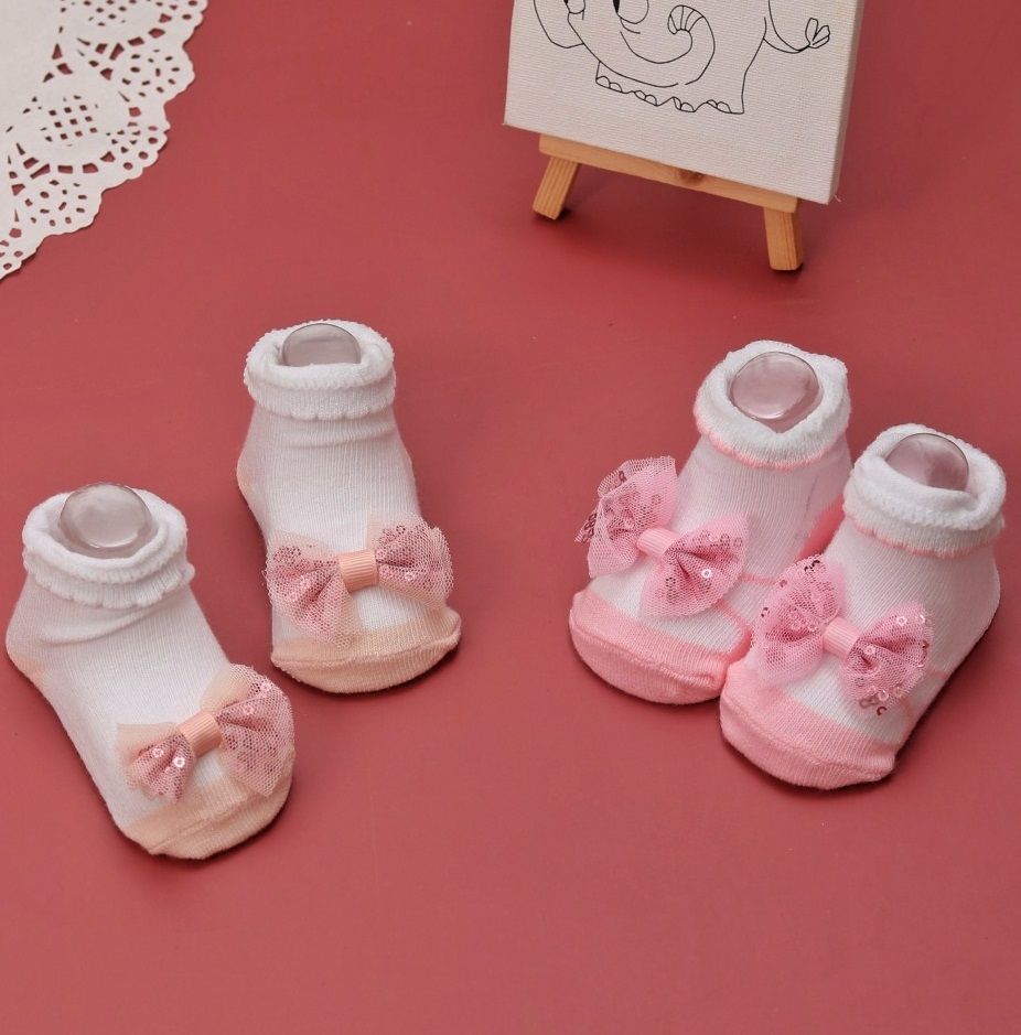 Arrangement of white, pink, and peach baby socks with bows, presented on a pink background