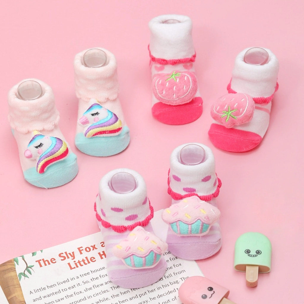 Assortment of baby socks with strawberry, cupcake, and unicorn designs on a pink backdrop