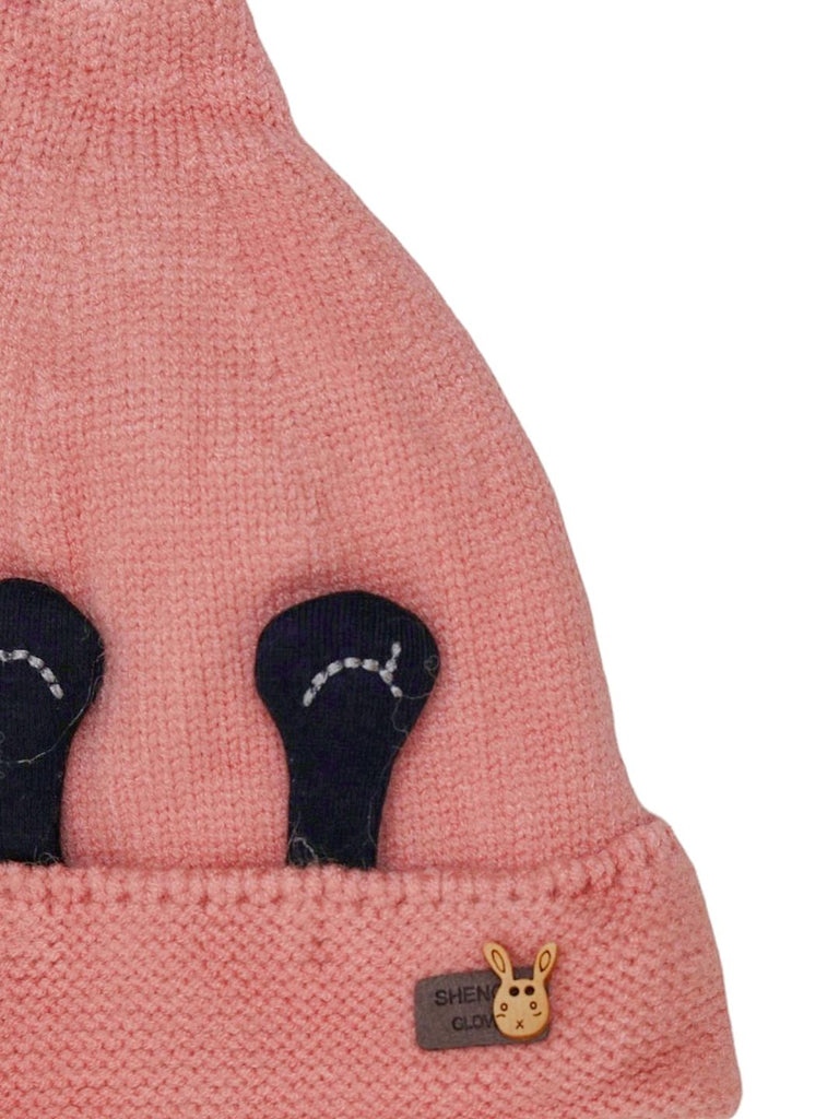 op view of a girl's winter beanie in pink with eye applique and soft pom-pom detail.
