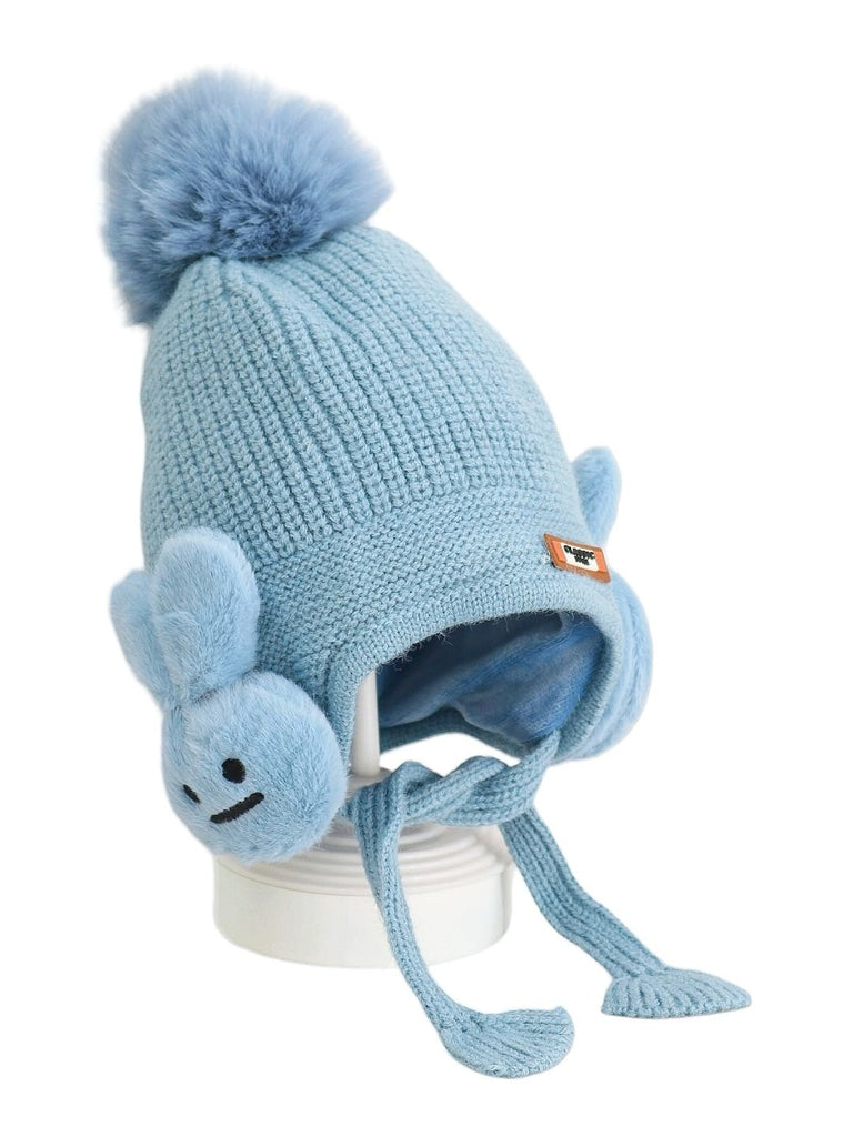 Side view of a blue knitted hat with bunny ear guards and fluffy pom pom.