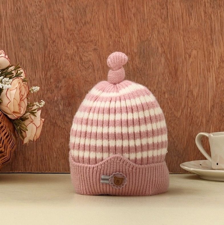 A charming dark pink and white striped beanie with a playful top knot, presented against a warm wooden background.