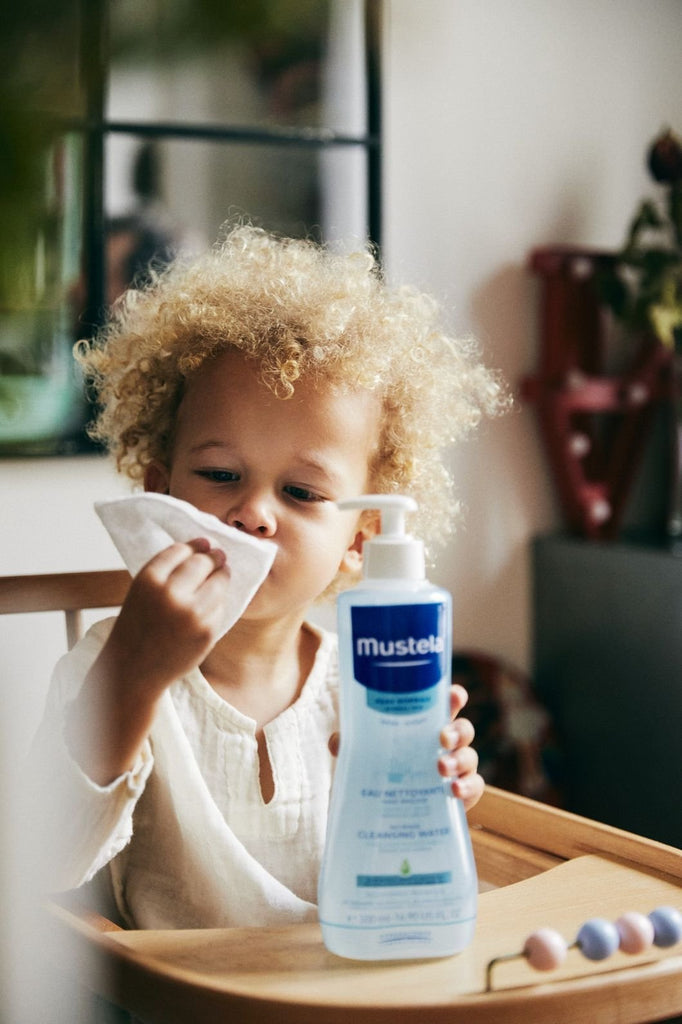 Curly-Haired Child Gently Wiping Face with Mustela Baby Cleansing Wate