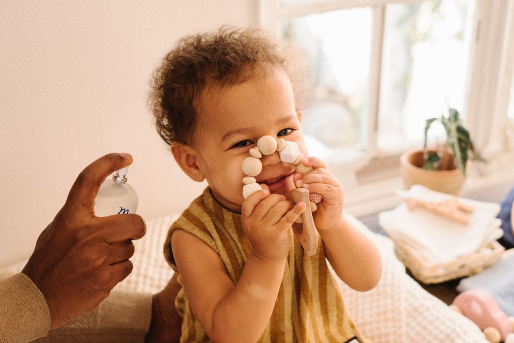 Cheerful baby holding Mustela Musti baby perfume, capturing the playful and gentle essence of the product.