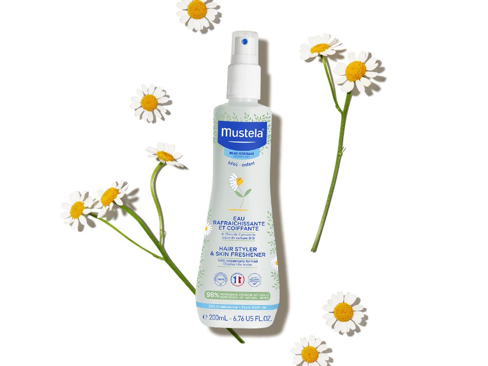 Mustela Hair Styler and Skin Freshener with chamomile flowers on a white background.