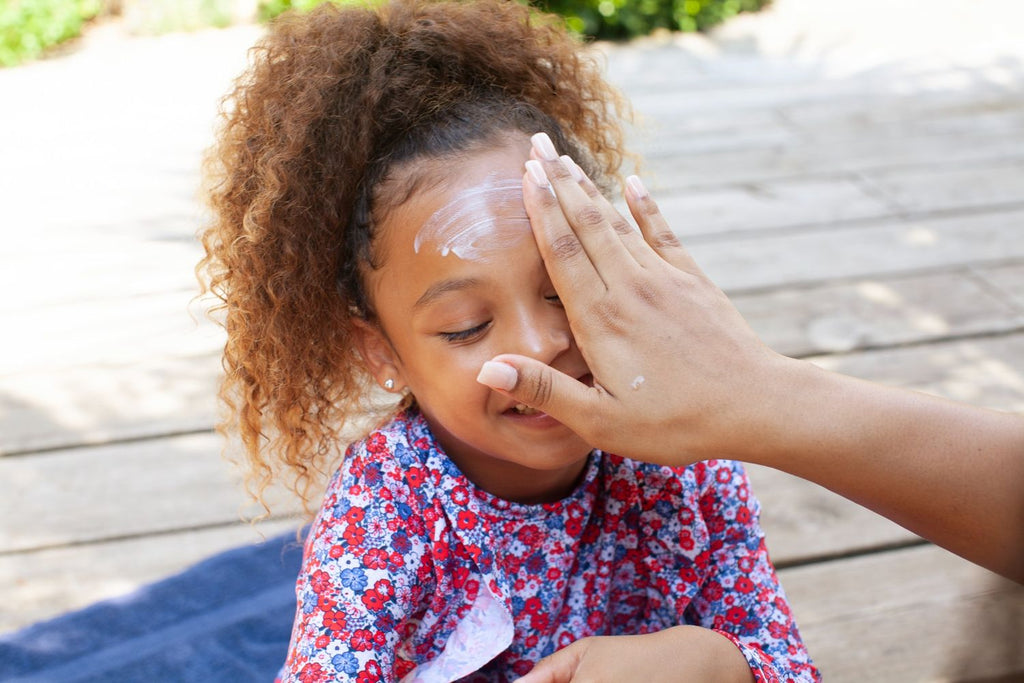 Parent applying Mustela Very High Protection SPF50+ Sun Lotion on smiling child outdoors