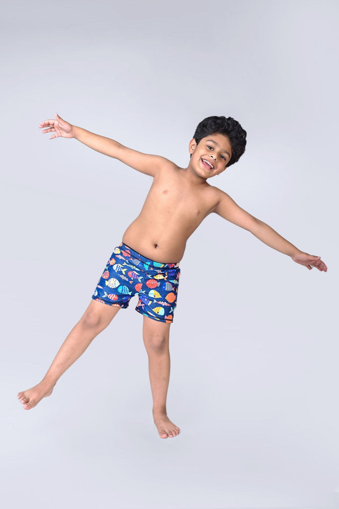 Happy boy with arms outstretched wearing navy blue fish print swim shorts