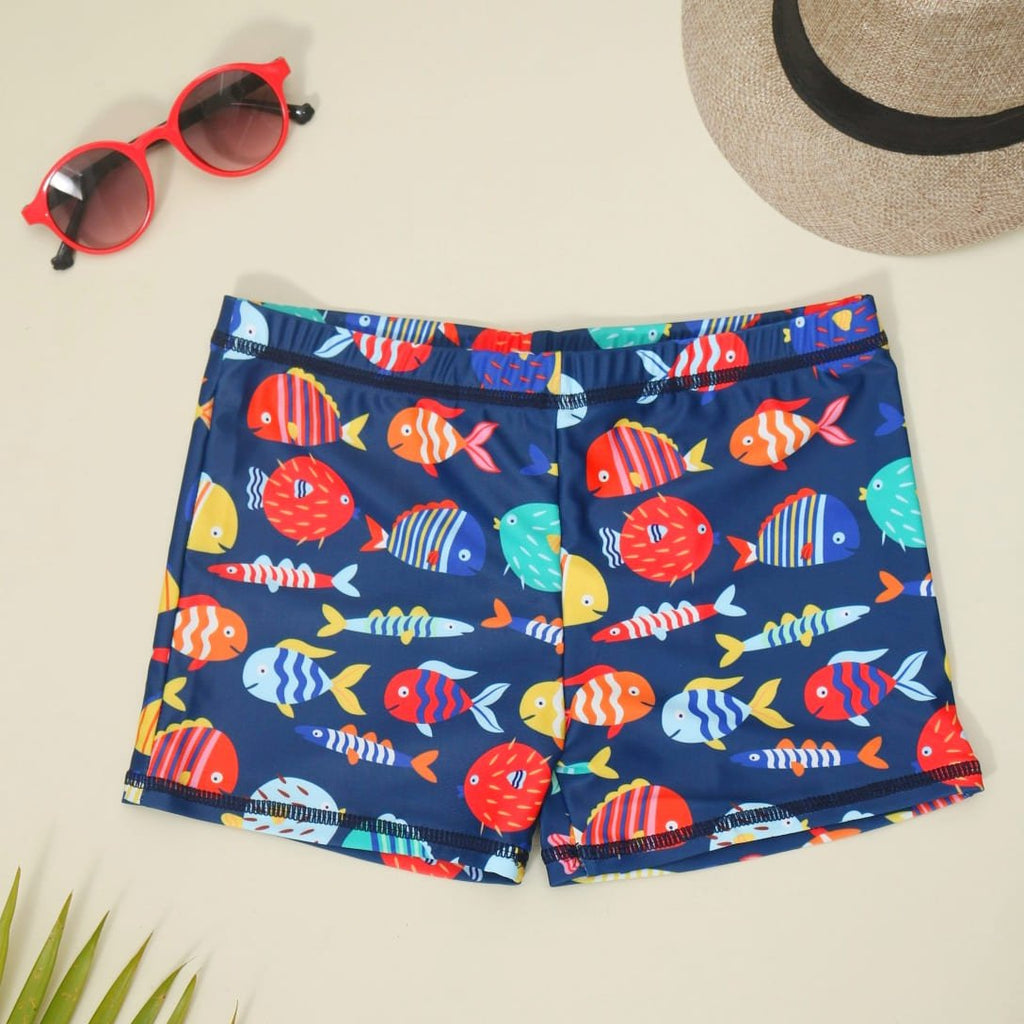 Navy blue fish print swim shorts laid out with summer beach accessories