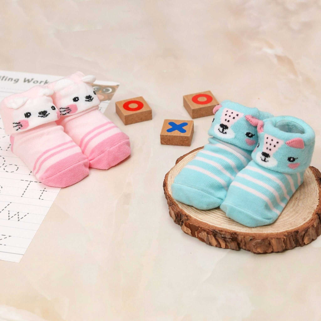 Baby girl socks with pink and white stripes, puppy face on one pair, and kitten face on the other, displayed with educational toys.