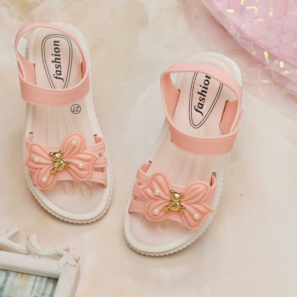 Adorable peach-coloured bow and bear sandals for toddlers on a soft pink background