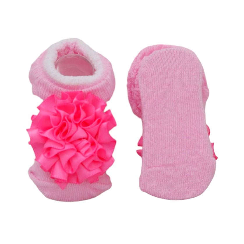 Baby girl socks with frilly pink flower decoration, showcasing the sole.