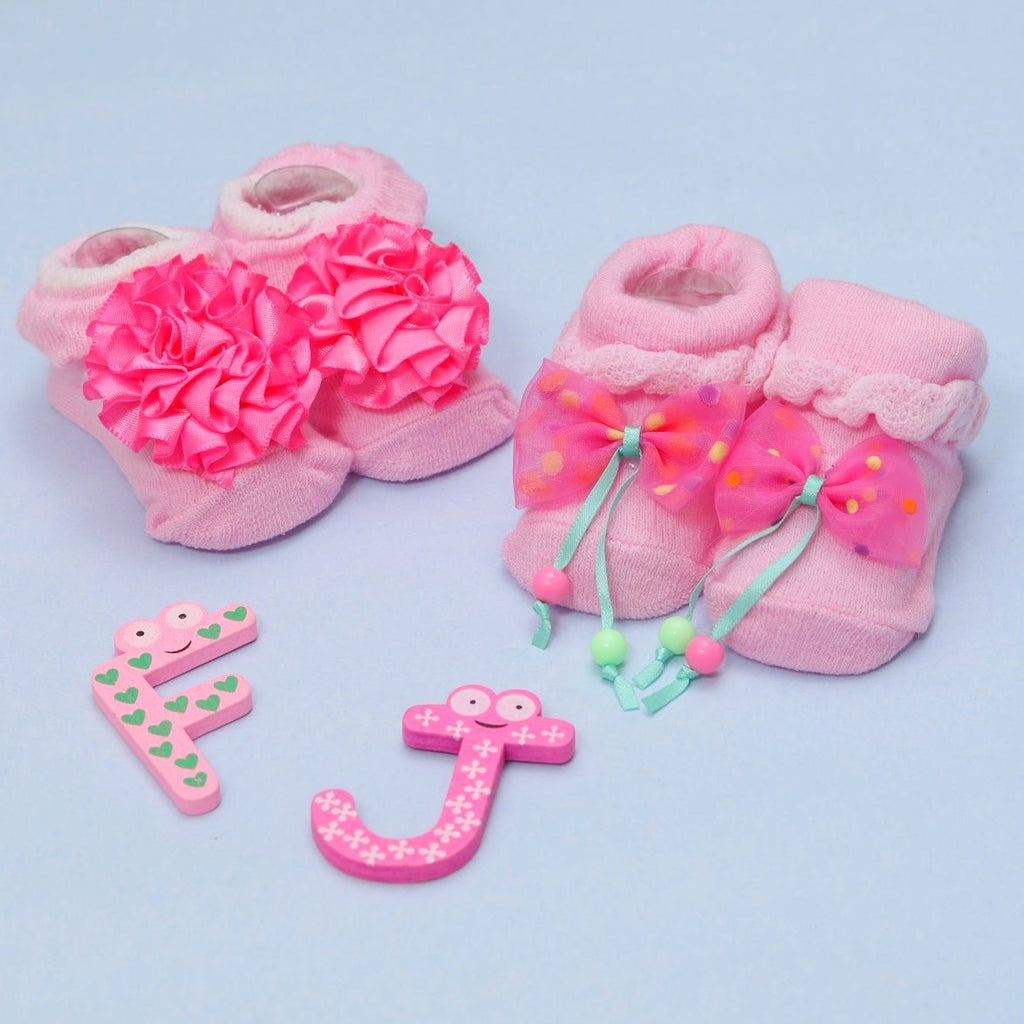 Baby girl socks with large pink flowers and polka-dot bows on a playful background with alphabet toys.