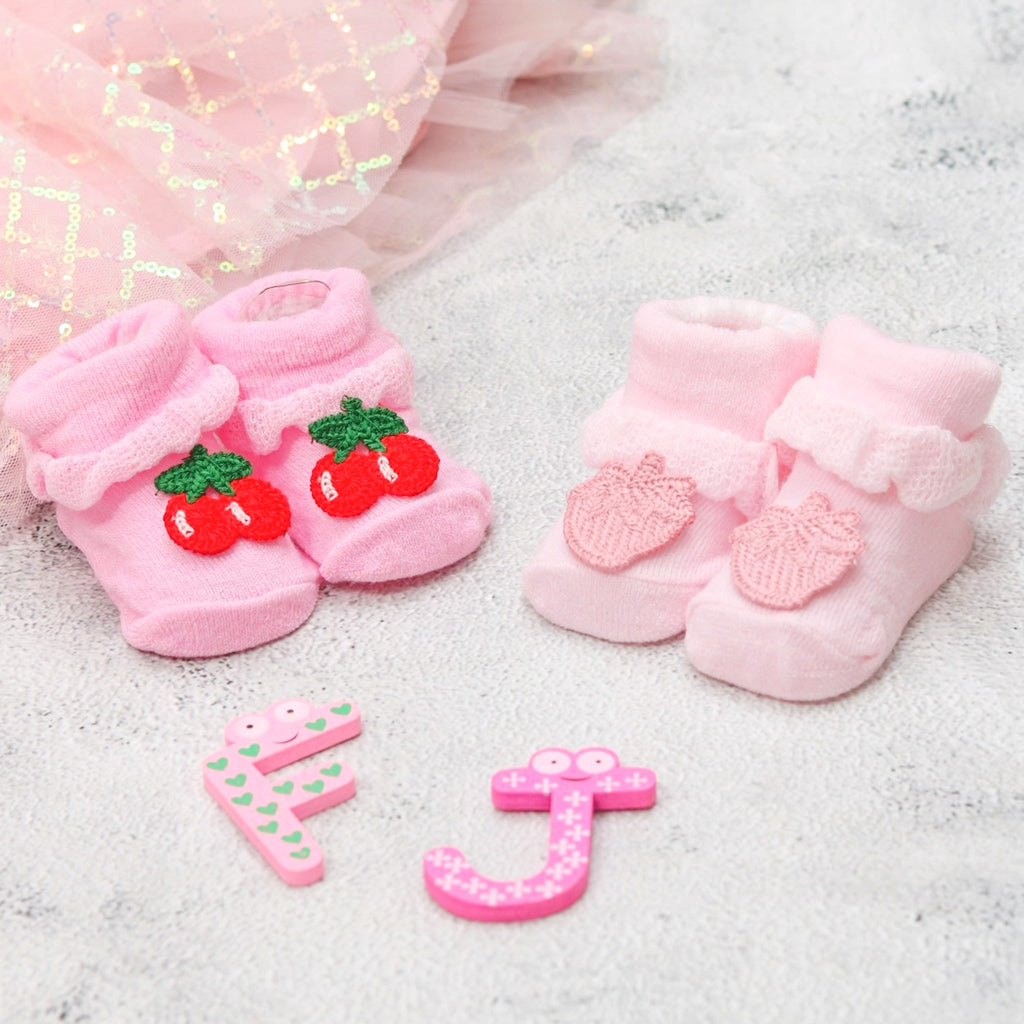 Baby girl's pink socks set with cherry and mango motifs, accompanied by playful number and letter toys.