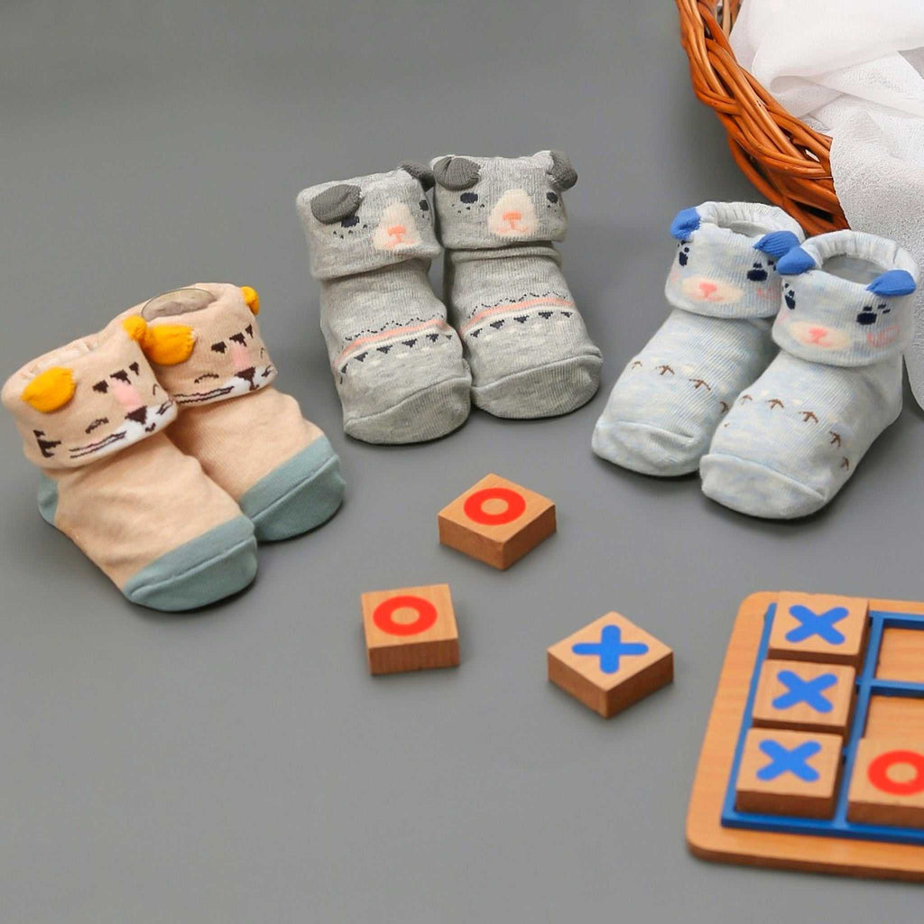 Array of Yellow Bee baby boys' socks with anti-skid animal designs, including bears and cows, next to children's wooden toys.