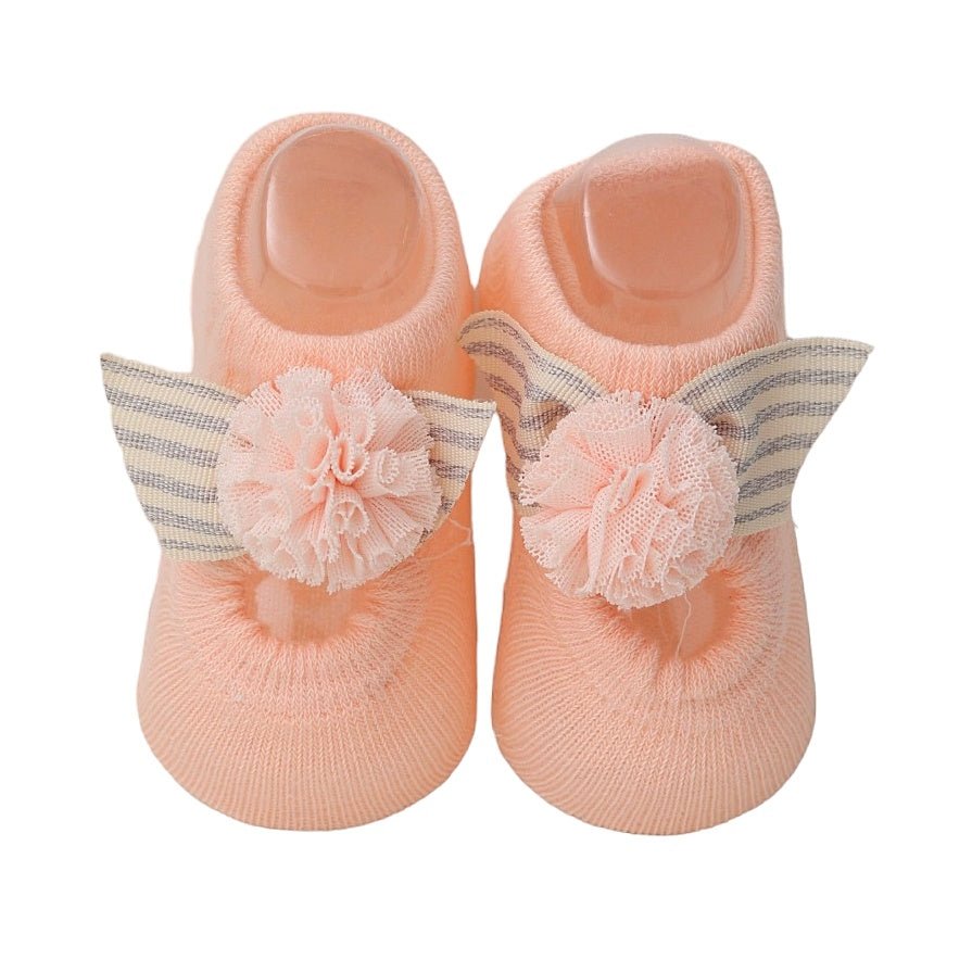 Close-up of peachy pink baby socks with lace pom-poms and plaid bows
